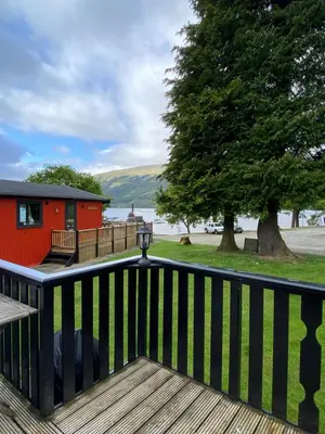 a deck with a red house and a tree at Cozy Loch Lomond Lodge 27, Rowardennan in Rowardennan