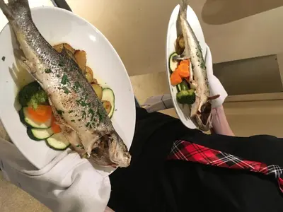 a person holding two plates of fish and vegetables at The Winnock Hotel in Drymen
