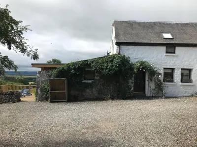 a white house with ivy growing on the side of it at The Old Barn - cottage with spectacular lake view in Port of Menteith