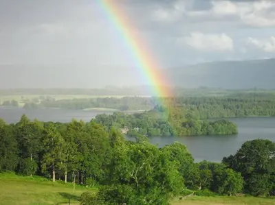 a rainbow over a lake with trees and forests at The Old Barn - cottage with spectacular lake view in Port of Menteith