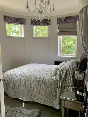 a bedroom with a bed and two windows and a chandelier at Pollokshields Burgh Hall Lodge Houses in Glasgow
