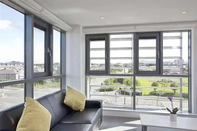 a living room with a leather couch and large windows at Edinburgh College Residence in Edinburgh