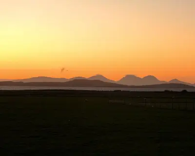 a sunset over a field with mountains in the background at Blaeberry Cottage in Killean