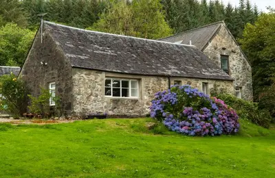 a stone house with flowers in front of it at Killean Farmhouse Cottages in Auchnangoul