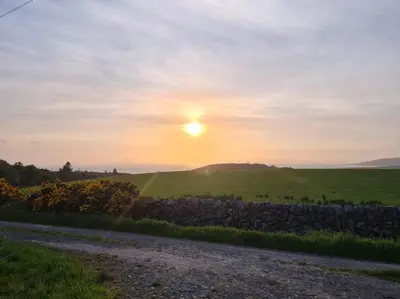 a sunset over a field with a stone wall at Kings Reach - Crinan Cottage in Lochgilphead