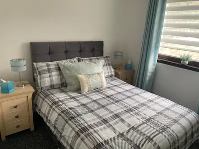 a bedroom with a bed with a plaid comforter and a window at Argyll Apartment Loch Lomond in Balloch