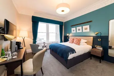 a bedroom with blue walls and a bed and a desk at The Perle Oban Hotel & Spa in Oban