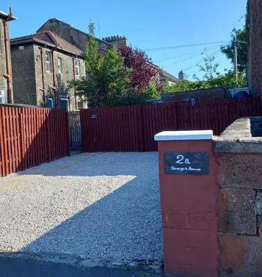 a red fence next to a driveway with a gate at J & S Apartments in Ayr