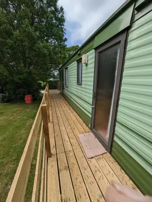 a large wooden deck next to a green trailer at 55 Glenfinart Caravan Park in Dunoon