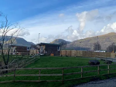 a barn with a fence and mountains in the background at Devon River Glamping Pods in Alloa