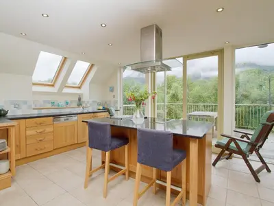 a kitchen with a island with blue chairs and windows at Carness West in North Ballachulish