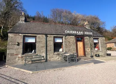 a stone building with a bench and tables in front of it at Cairnbaan House in Cairnbaan