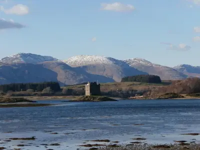 a castle in the middle of a river with mountains in the background at Glenview in Appin