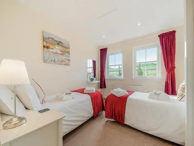 two beds in a room with red curtains at Buzzard Cottage - 27940 in Stirling