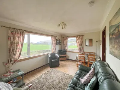 a living room with a couch and a large window at Gean Cottage in Powmill