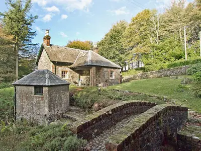 an old stone house on a hill with a stone wall at Gardener's Cottage-Uxt in Corsock
