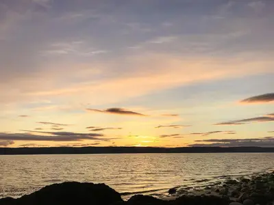 a sunset over a body of water with rocks at Dunmaghlas in Pirnmill
