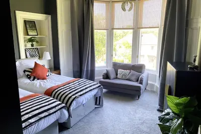a bedroom with two beds and a chair and a window at Stunning 3 bedroom Victorian home near Pollok country park in Glasgow