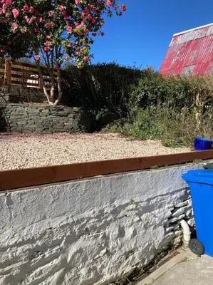 a retaining wall with a tree and a blue trash can at The Villas in Helensburgh