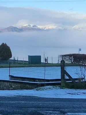 a fence next to a body of water with snow covered mountains at The Villas in Helensburgh