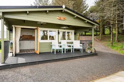 a green house with a table and chairs on a porch at Torr Lodge- luxury log cabin with private hot tub! in Ballycastle