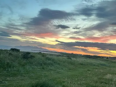 a sunset over a field of grass with the sky at Seaside Home in Ardeer Square