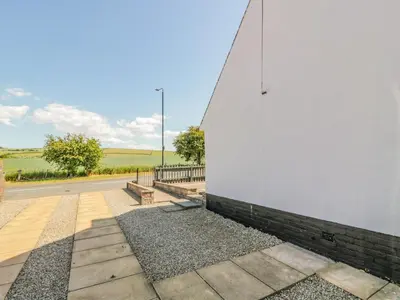 a white wall with a bench next to a road at 22 Turnberry Road in Girvan
