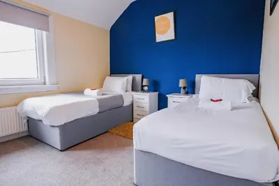 a bedroom with two beds and a blue wall at West Apartment in Coatbridge