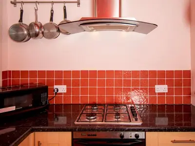 a kitchen with a stove and red tiles on the wall at Private Entrance GF 2 bed flat near Renfrew Centre - Pass the Keys in Renfrew