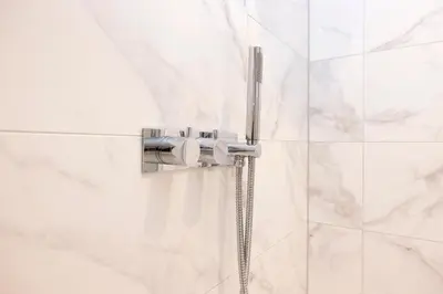 a shower head in a bathroom with white tiles at Deluxe 3-bedroom Apartment on Princes Street overlooking Edinburgh Castle in Edinburgh