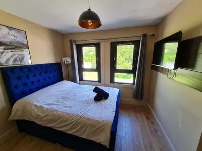 a bedroom with a bed with a blue headboard and two windows at Kinlochleven Holiday Home in Kinlochleven