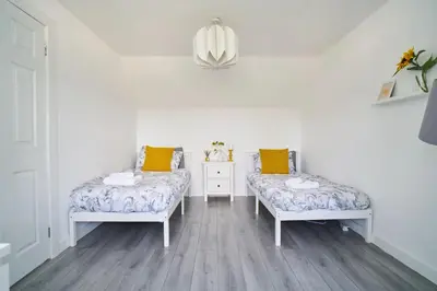 two beds in a room with white walls and wooden floors at Woodside Apartment in Coatbridge