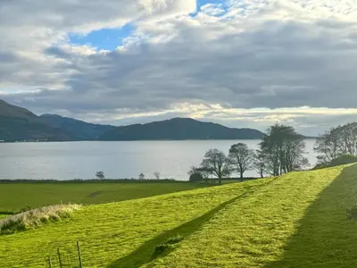 a grassy field with a view of a lake at Ash, Birch and Rowan Self Catering Cabins in Onich
