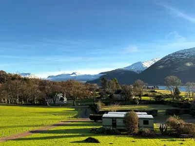 a house in a field with mountains in the background at Ash, Birch and Rowan Self Catering Cabins in Onich