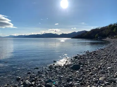 a rocky shore of a lake with the sun in the sky at Ash, Birch and Rowan Self Catering Cabins in Onich