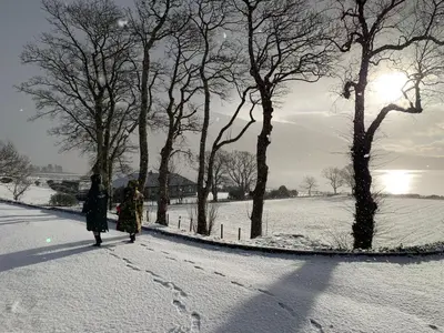 two people walking down a snow covered road with trees at Ash, Birch and Rowan Self Catering Cabins in Onich