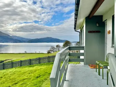 a house with a balcony with a view of a lake at Ash, Birch and Rowan Self Catering Cabins in Onich