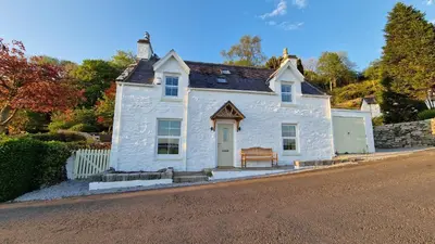 a white house with a bench on the side of a street at Nordlys Cottage in Newton Stewart