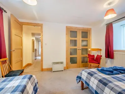 a bedroom with two beds and a chair and a window at Brondeg Lodge in Crarae