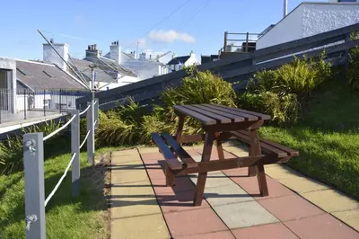 a wooden picnic table and a bench on a sidewalk at Seal Cottage in Portnahaven