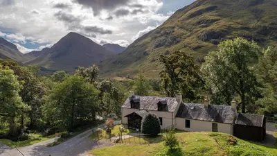 a house on a hill with mountains in the background at Heart of Glencoe Holidays in Glencoe