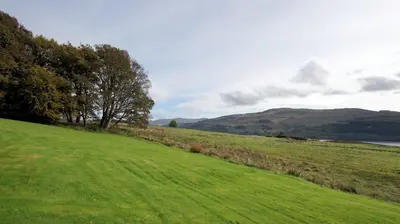 a green field with trees and a lake in the background at Morenish Mews Killin Cottage in Morenish