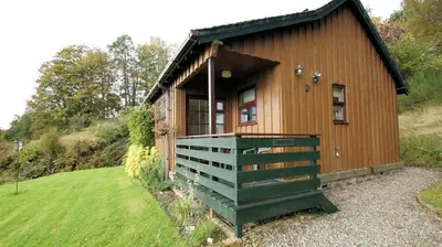 a small wooden cabin with a green porch in a field at Morenish Mews Kenmore Cottage in Morenish