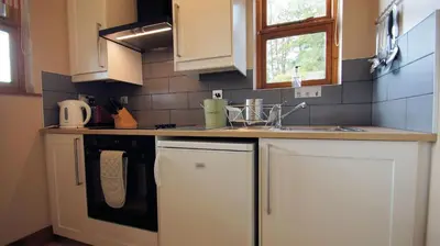 a kitchen with white cabinets and a black dishwasher at Morenish Mews Kenmore Cottage in Morenish