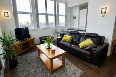 a living room with a black leather couch and a coffee table at Penthouse Apartment in Stirling