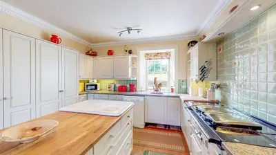 a kitchen with white cabinets and a wooden counter top at Airds of Kells House in Castle Douglas