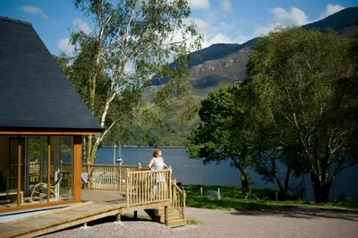 a woman standing on a wooden deck next to a lake at Lochleven Seafood Cottage in Onich