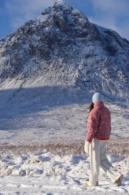 a woman walking in the snow in front of a mountain at Woodlands House with Hot Tub in Ballachulish
