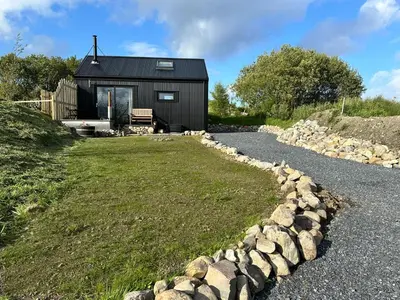 a small black house with a gravel driveway at Jura - The Black Hut in Isle of Jura