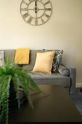 a clock on the wall above a couch with pillows at McCracken House in Uddingston